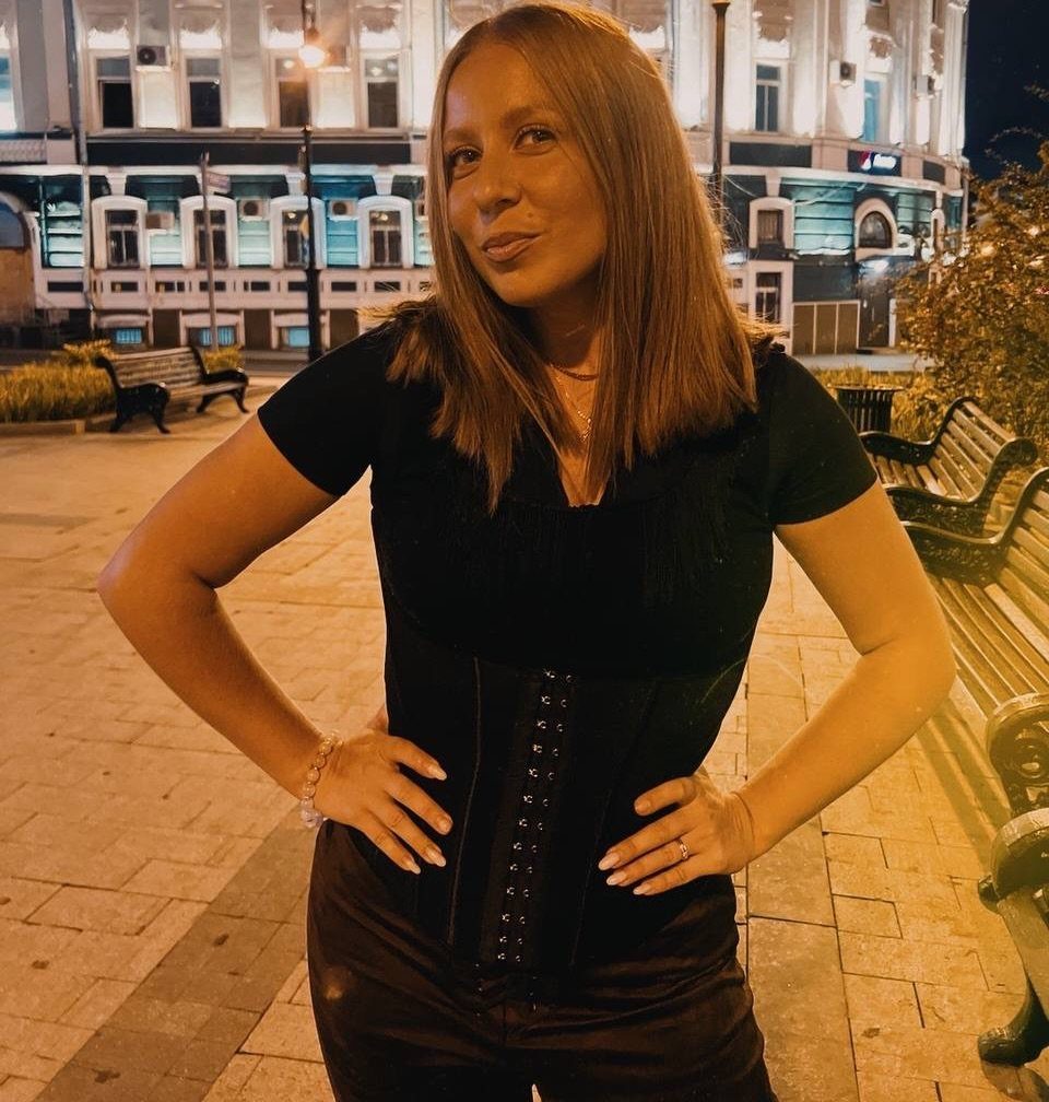 Woman wearing a black corset top and matching black pants posing outdoors at night.