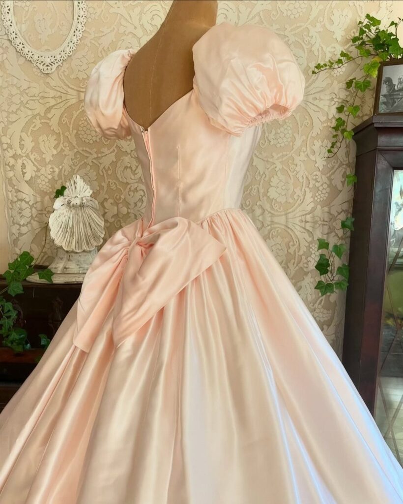 Pale pink satin evening gown with puff sleeves and a large back bow.