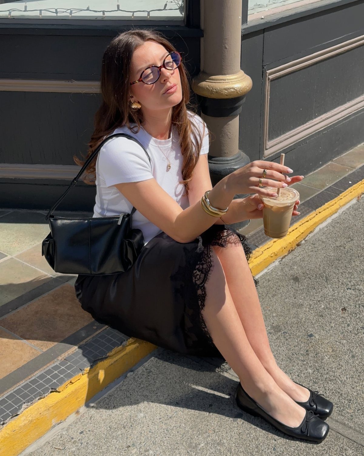 Woman in white t-shirt and black lace-trim skirt sitting on a city sidewalk