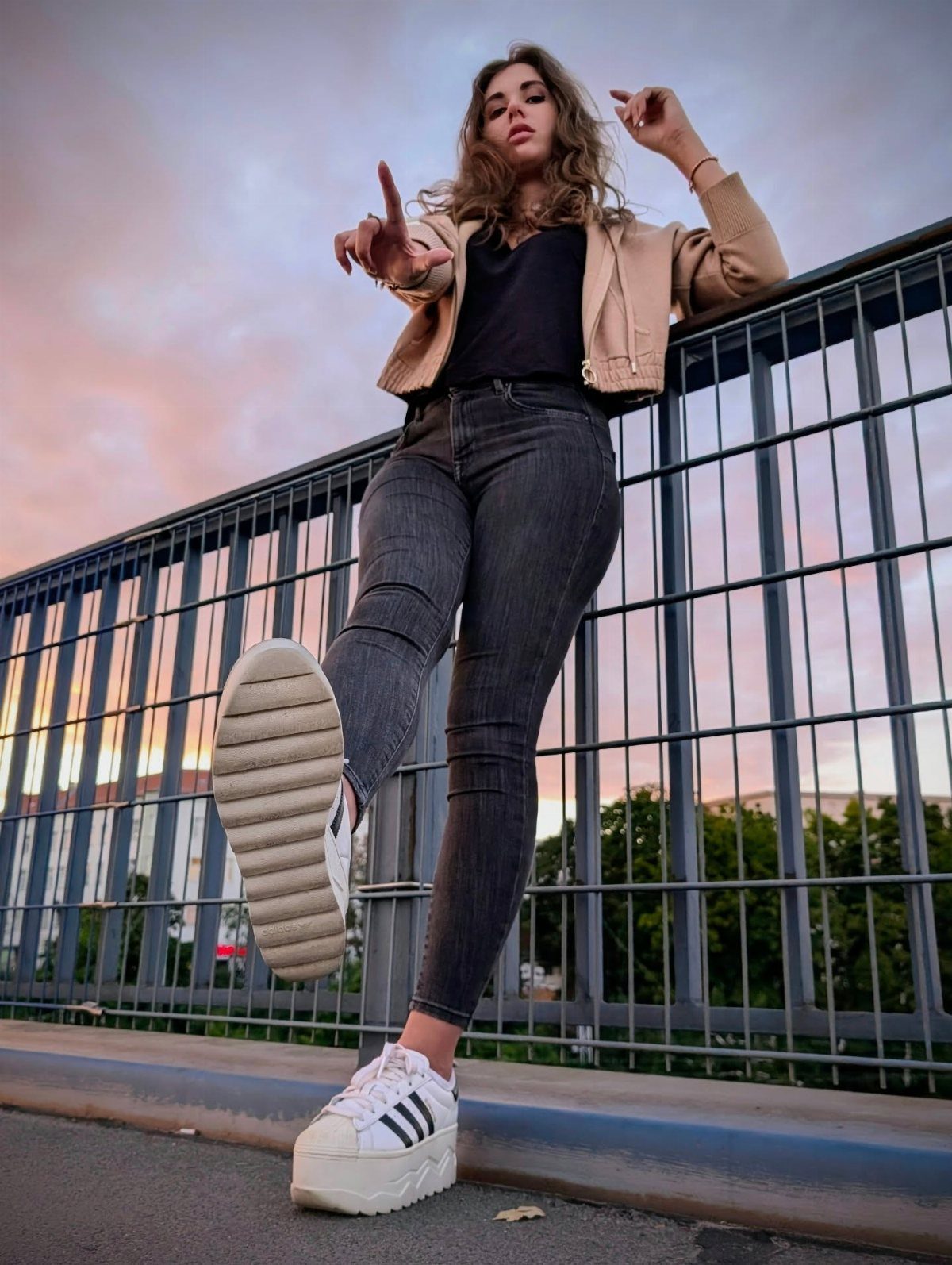 Woman in grey jeans and white platform Adidas sneakers posing by a railing