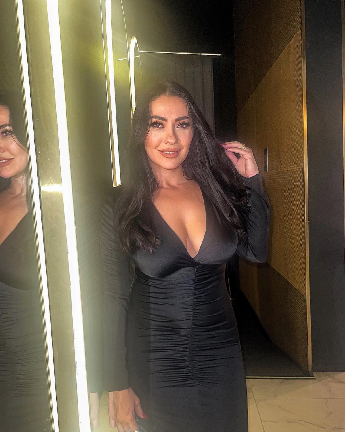 Woman wearing a tight, long-sleeved black dress with ruched detailing and V-neckline.