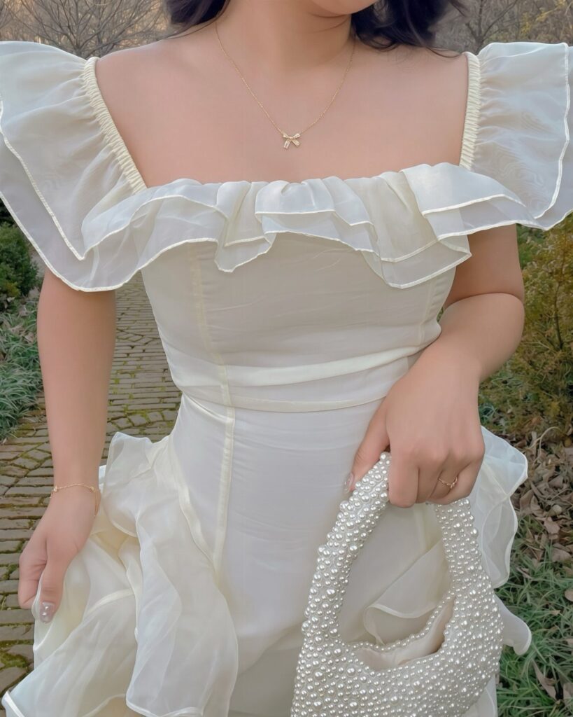 Person wearing a white flowy ruffled dress and holding a beaded handbag outdoors.