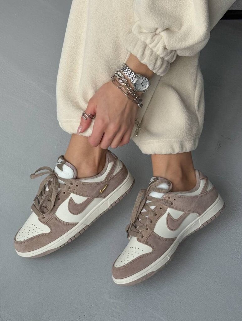 Beige and white Nike Dunk sneakers worn with cream trousers on grey concrete.