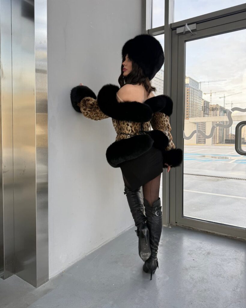 Woman in black mini dress with leopard print fur jacket and fur hat.
