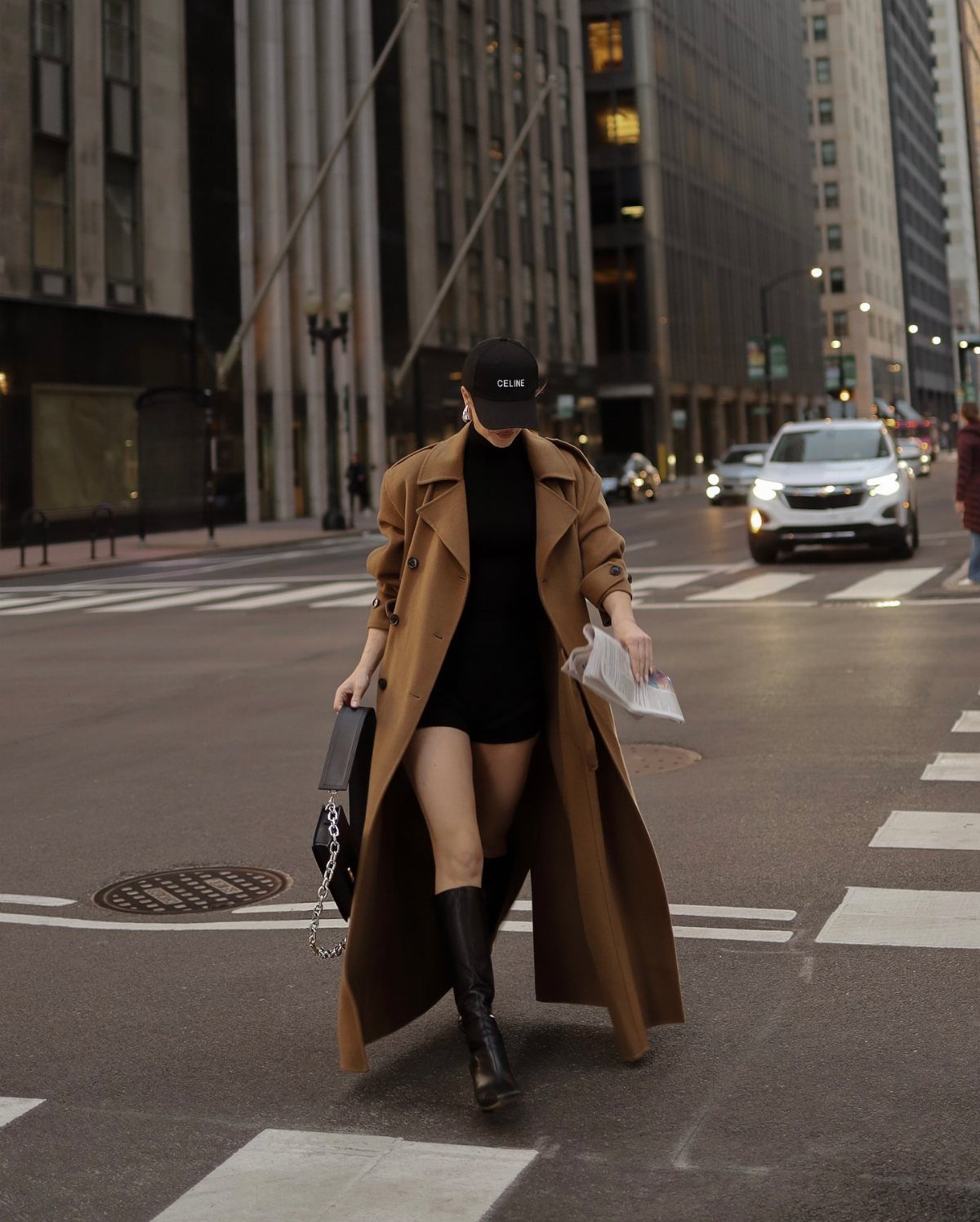 Person in tan trench coat and black dress wearing black leather boots.