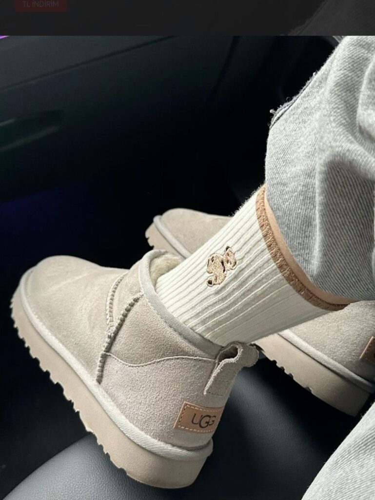 Beige UGG mini boots worn with white socks and grey jeans in a car.