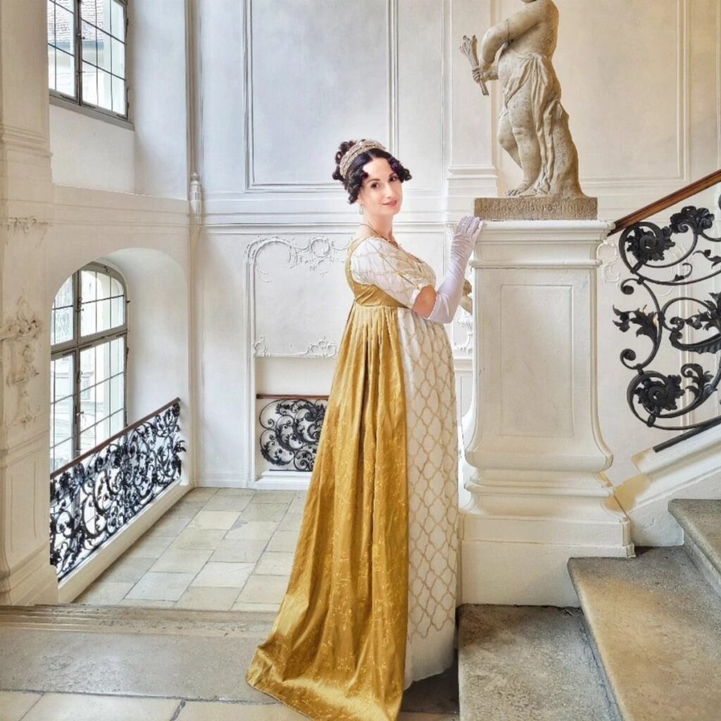 Woman in a gold and white Regency era empire waist gown in a palace.