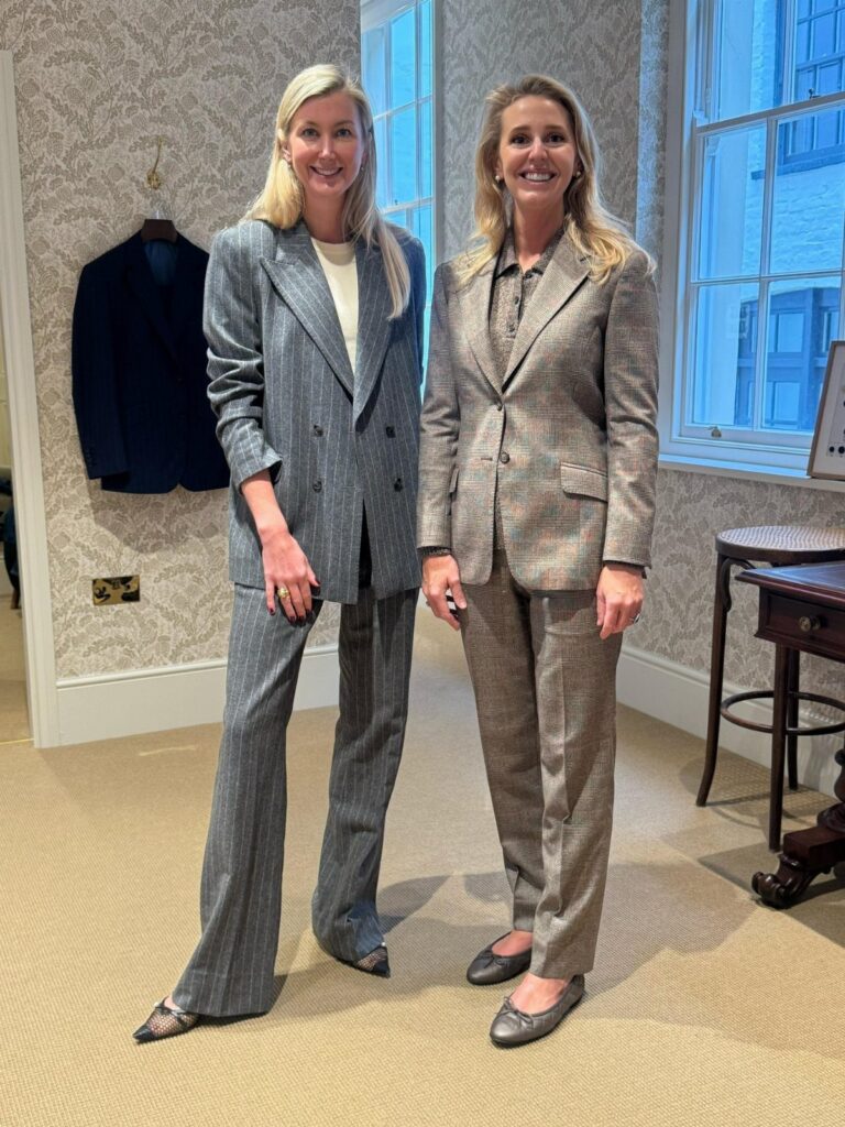 Two women wearing professional tailored trousers and matching blazers in a bright room.