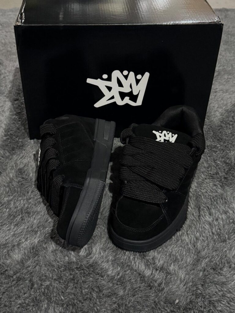 Black suede sneakers with thick chunky laces in front of a black box.