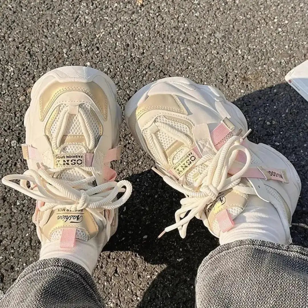 Chunky white and cream streetwear sneakers with pink accents on grey asphalt.