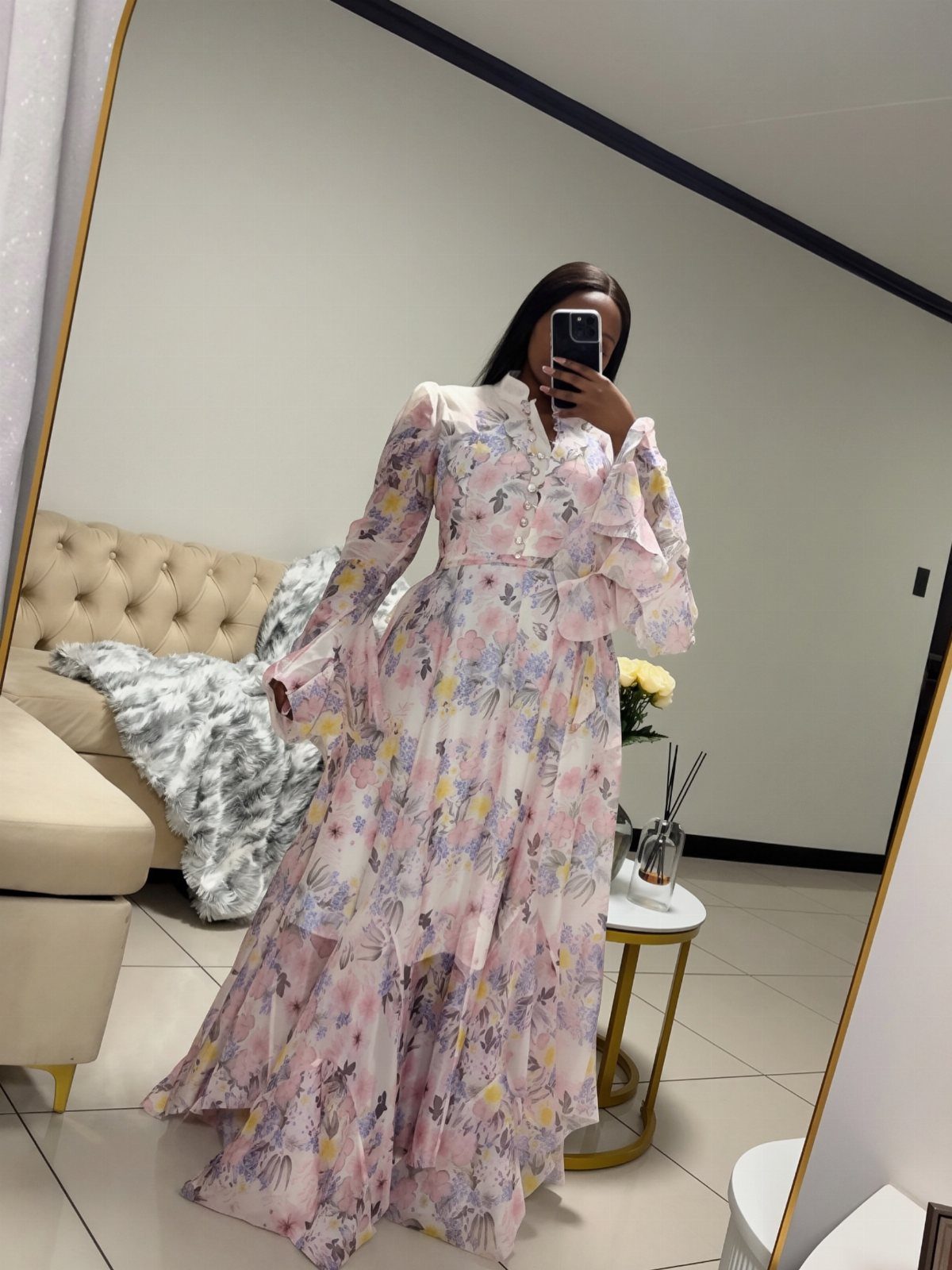 Woman in a floral print maxi dress taking a mirror selfie in a room.