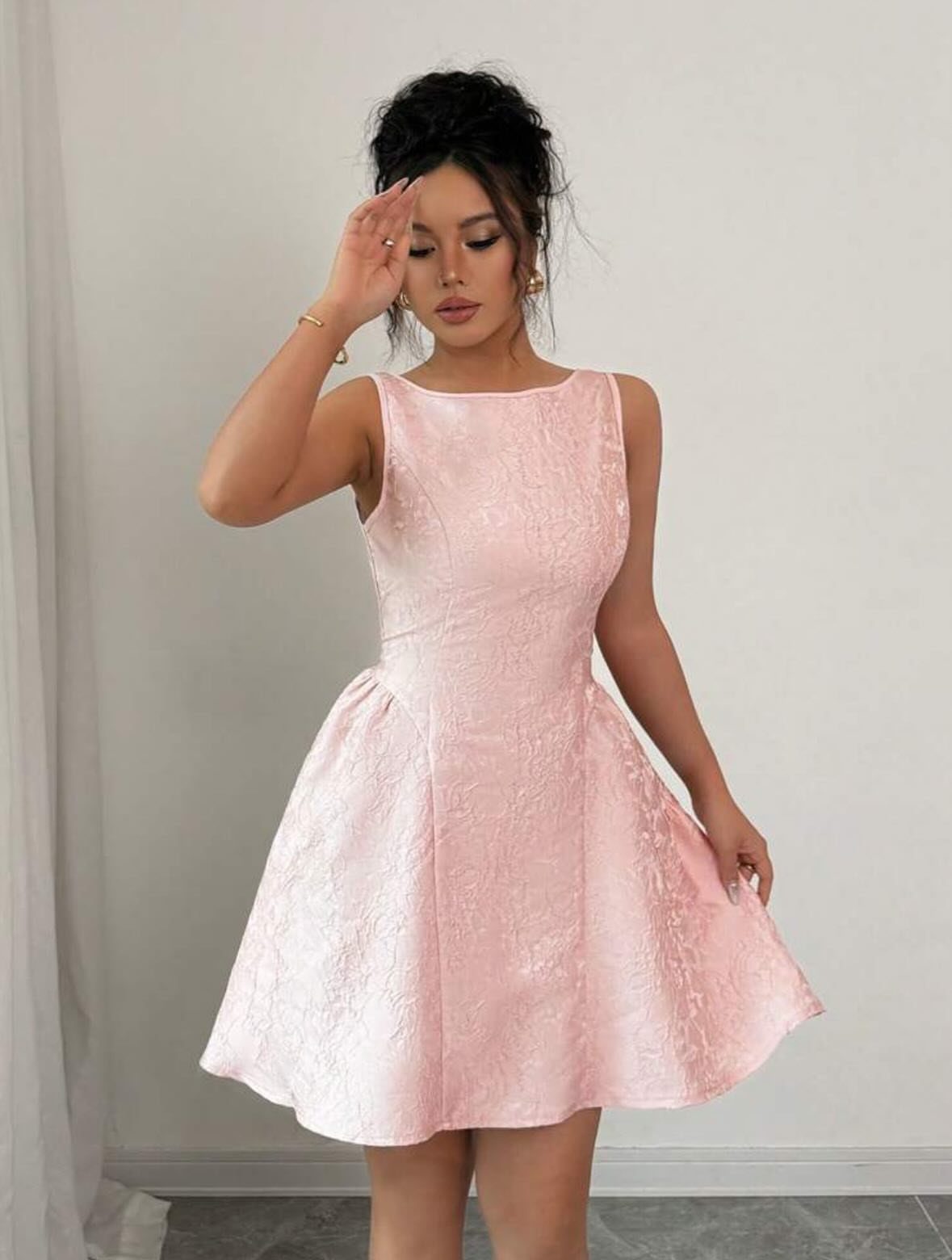 Woman wearing a short, sleeveless, elegant light pink satin dress with flared skirt.