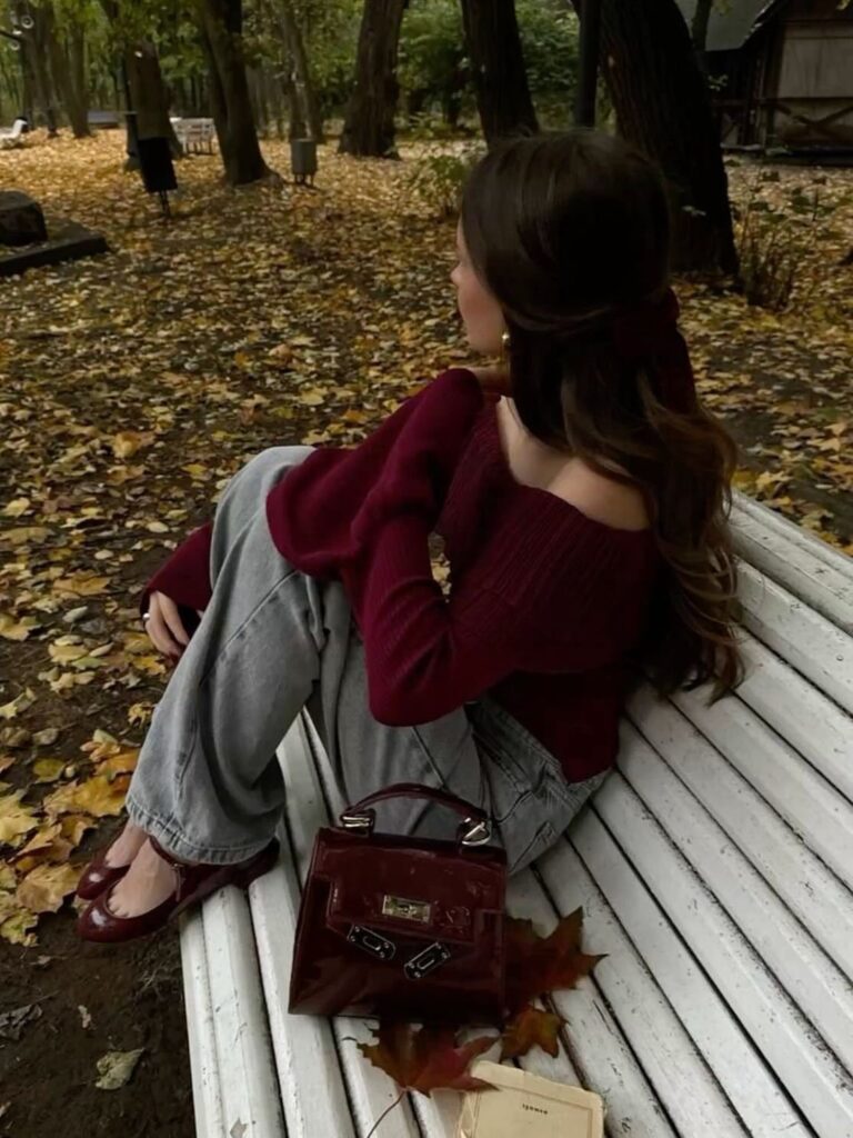 Woman in burgundy sweater and jeans sitting on a bench in autumn park
