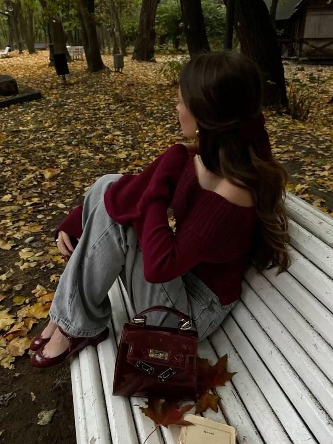 Woman in burgundy sweater and jeans sitting on a bench in autumn park