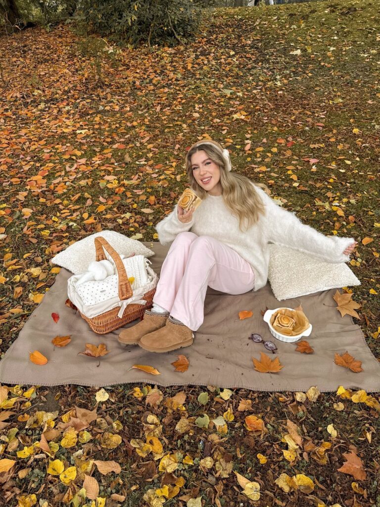 Woman in a white fluffy sweater and pink pants enjoying a fall picnic.