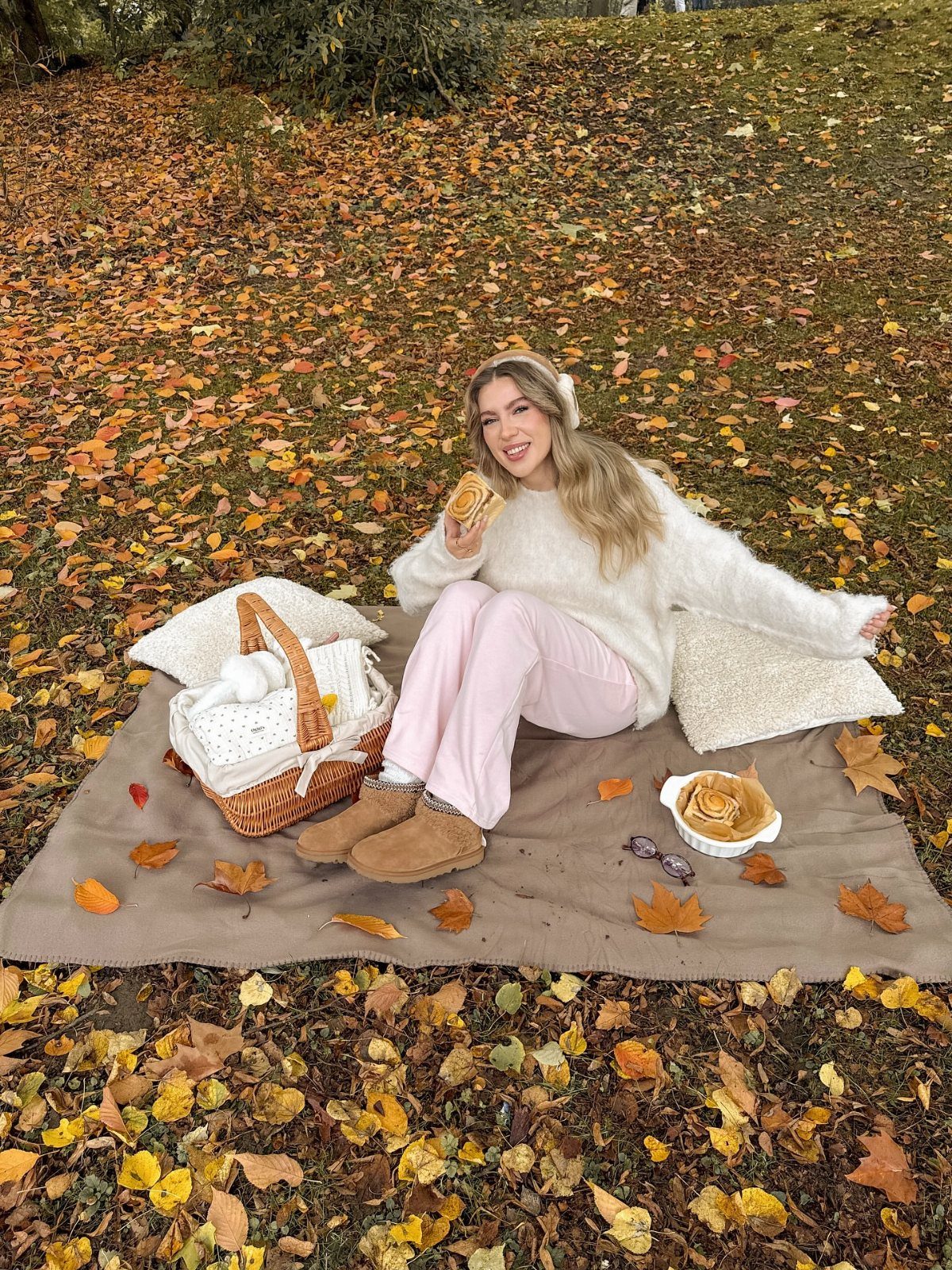 Woman in a white fluffy sweater and pink pants enjoying a fall picnic.