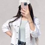 Person wearing a white denim jacket and blue skinny jeans taking a selfie.