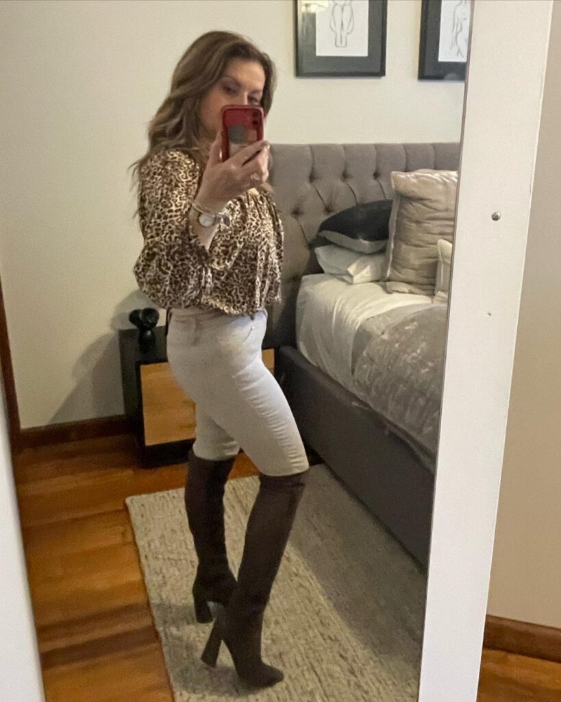 Woman wearing leopard print blouse, light pants, and tall brown heeled boots.