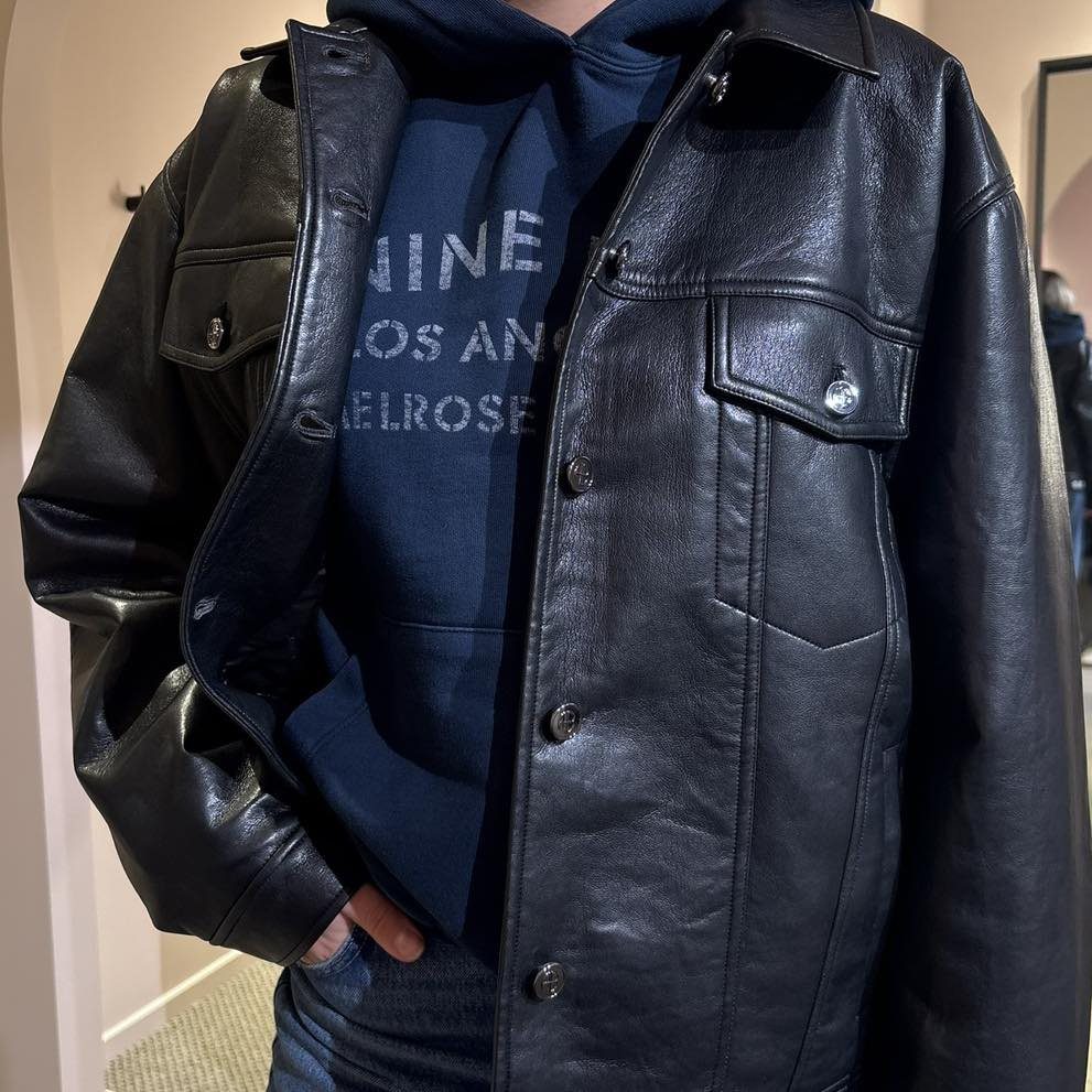 Black leather jacket layered over a navy blue hoodie and blue jeans.