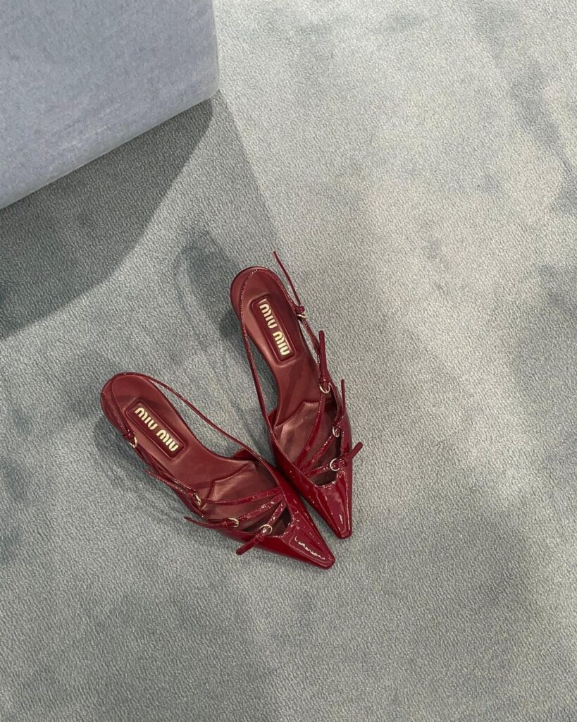 Dark red glossy Miu Miu kitten heels with straps on grey carpet.