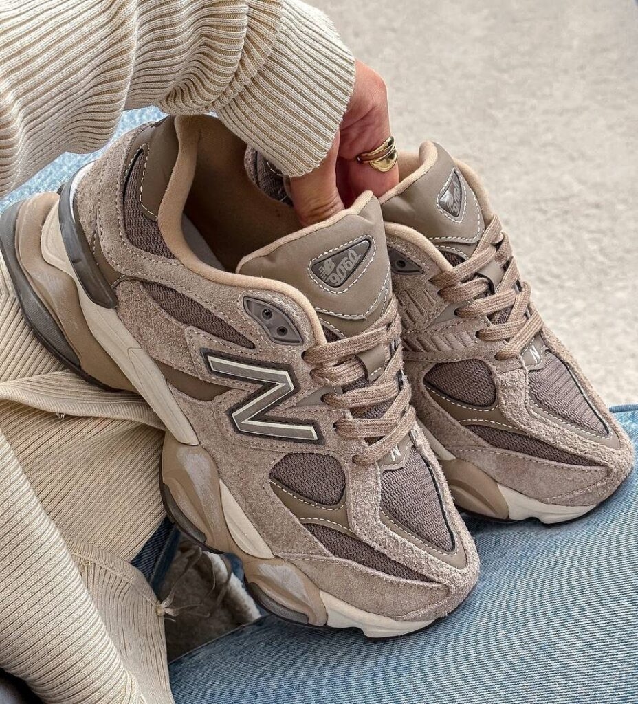 Beige New Balance 9060 sneakers held by a person wearing a ribbed sweater.
