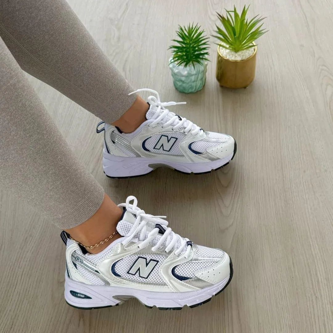 White New Balance sneakers with silver details worn with grey trousers on wood floor