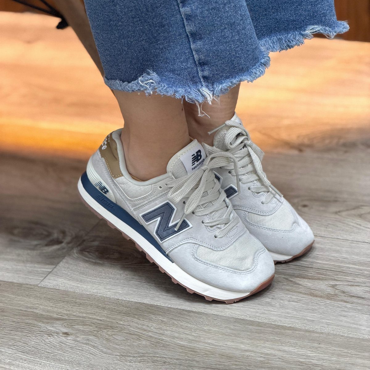 Light grey New Balance sneakers with blue accents worn with frayed blue jeans.