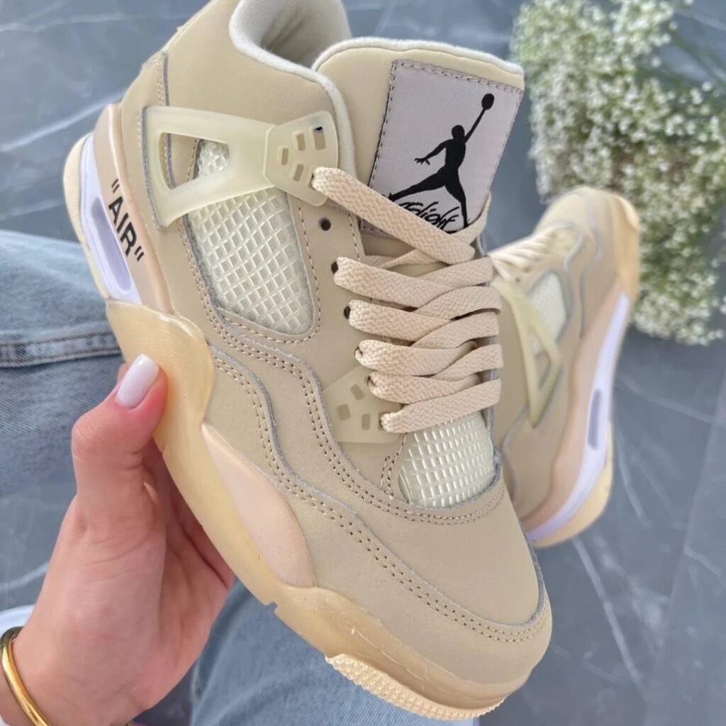 Cream Air Jordan 4 Off White Sail sneakers held by a hand.