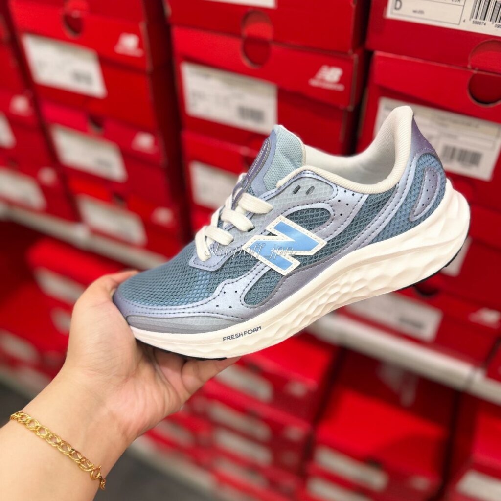 Light blue New Balance sneaker held in hand against red shoe boxes background