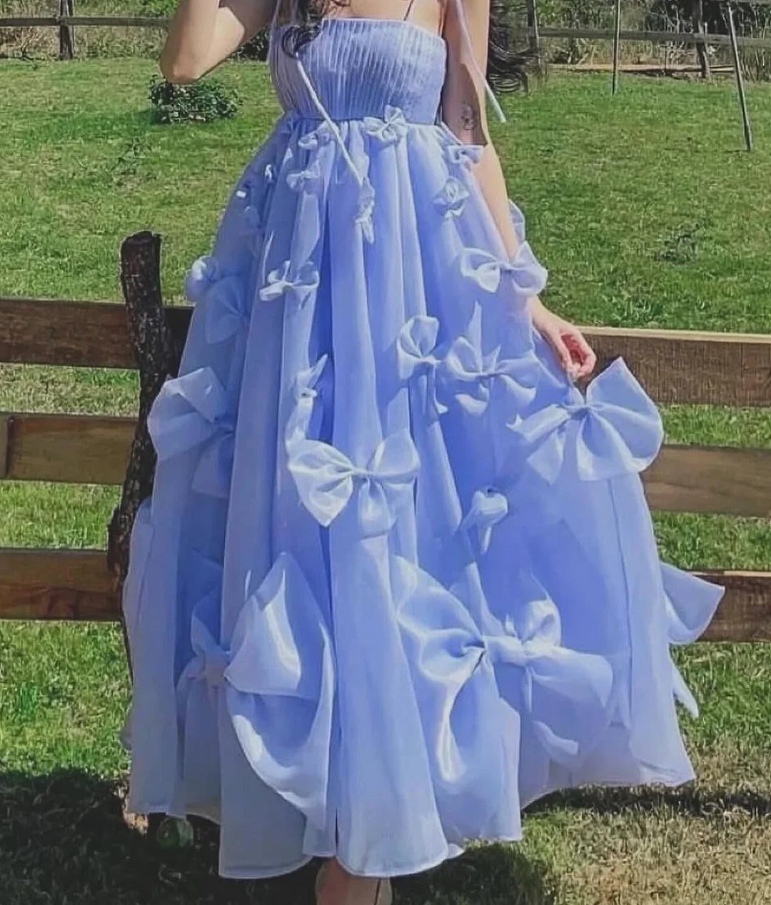Light blue sleeveless tulle dress with large bows on the skirt in a field
