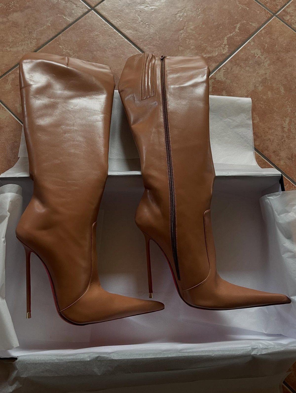 Brown leather high-heeled boots with pointed toes inside a white shoebox.
