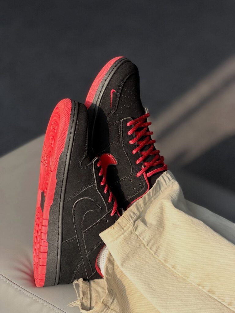 Black Nike sneakers with red laces and soles worn with beige corduroy pants.