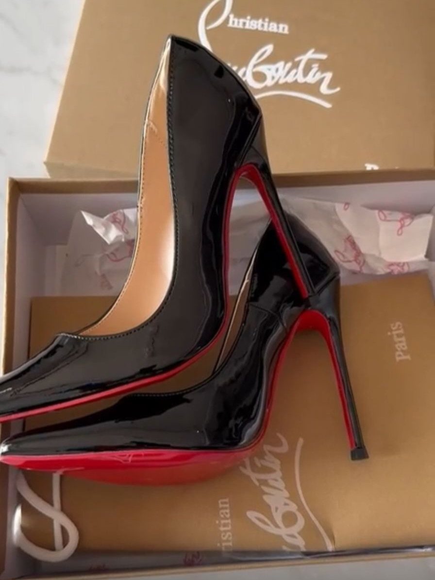 Black patent leather high heels with red soles inside a branded shoe box.