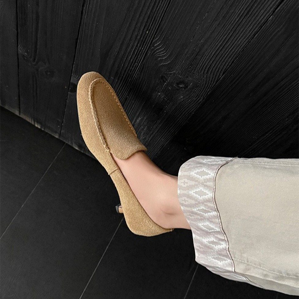 Tan round toe kitten heels worn with light trousers against a dark background