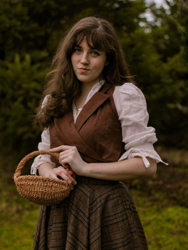 Woman in vintage country attire with a brown vest and woven basket outdoors.