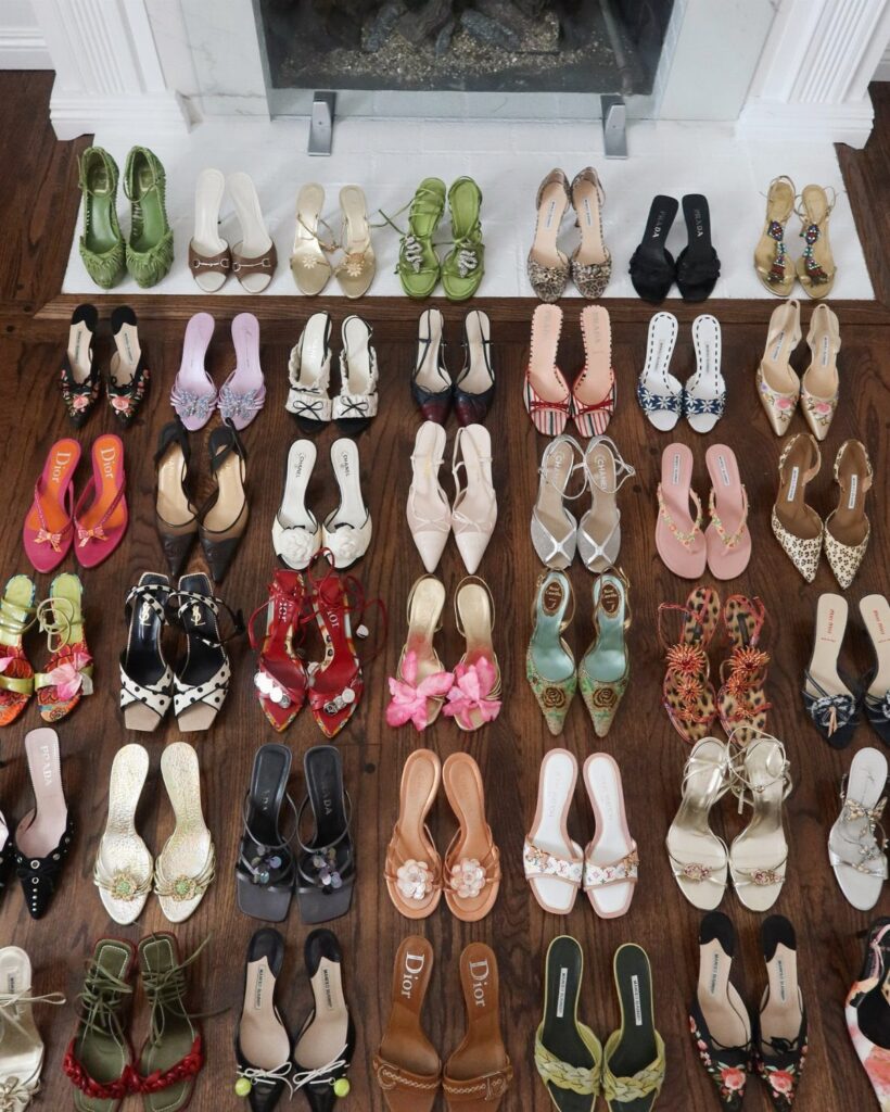 Many pairs of colorful vintage high heels and sandals arranged on a wooden floor.