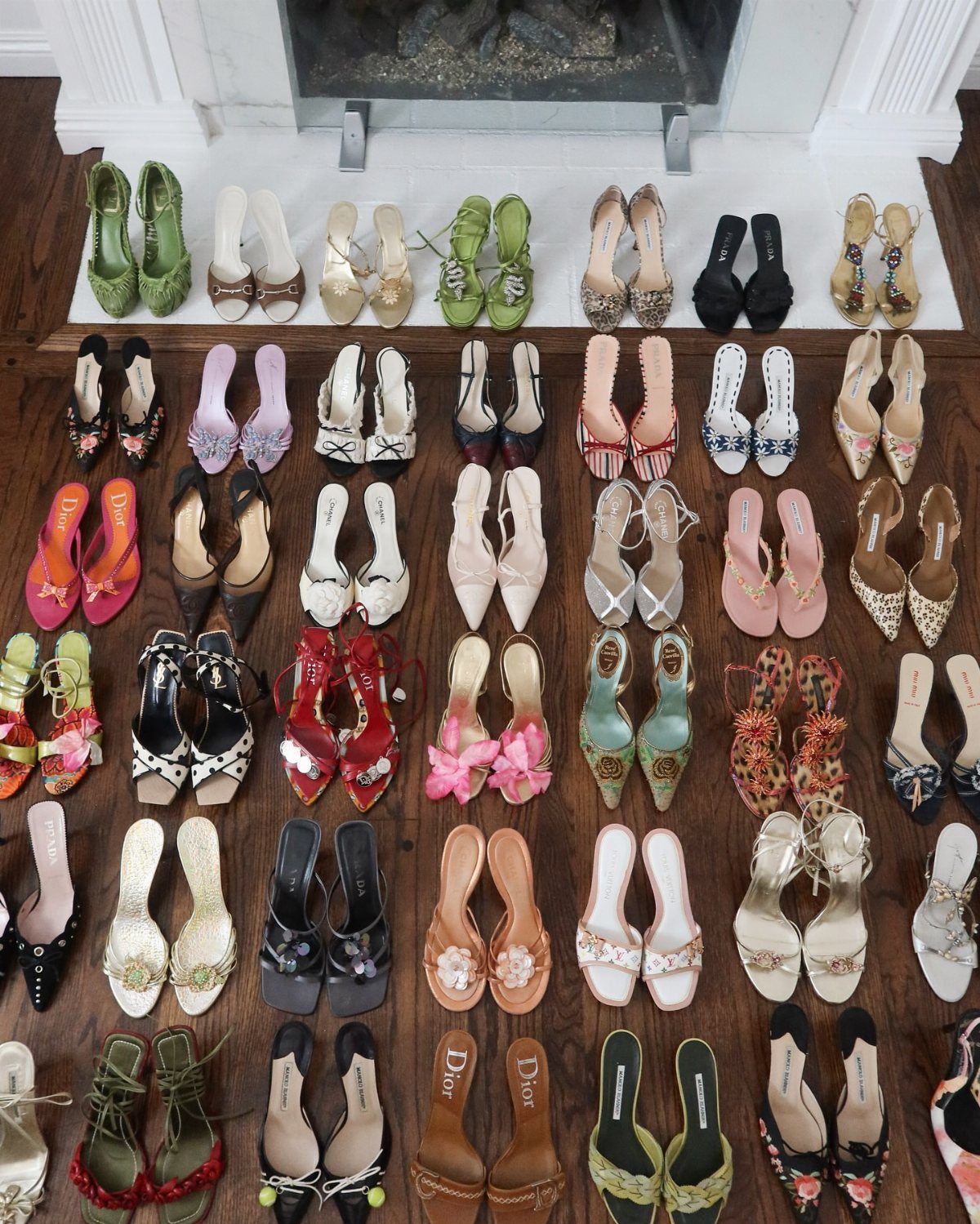Many pairs of colorful vintage high heels and sandals arranged on a wooden floor.