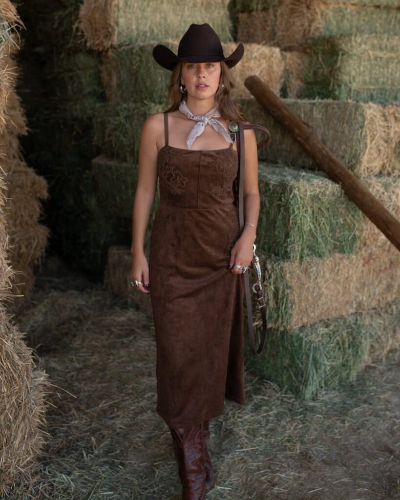 Woman in brown cowboy hat and suede dress standing by hay bales