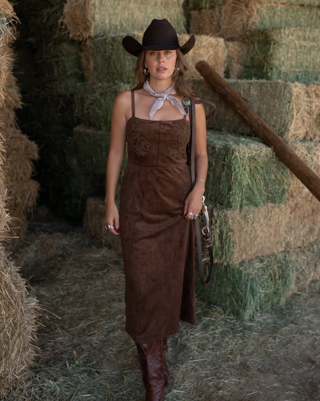 Woman in brown cowboy hat and suede dress standing by hay bales